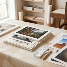 Fine art paper prints and photo prints arranged on a warm studio worktable.